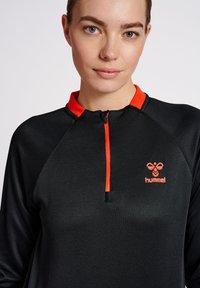 Top sportivo nero con collo a zip e vivaci accenti arancioni. Tessuto testurizzato con logo sul lato sinistro.
