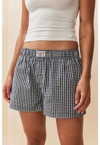 Short en gingham bleu marine et blanc avec une taille élastique, devant plat et poches latérales, confectionné dans un tissu léger. Étiquette de la marque visible.
