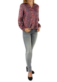 Multicolored blouse with a V-neck, long sleeves, and a loose fit, paired with light grey skinny jeans and black flat shoes.