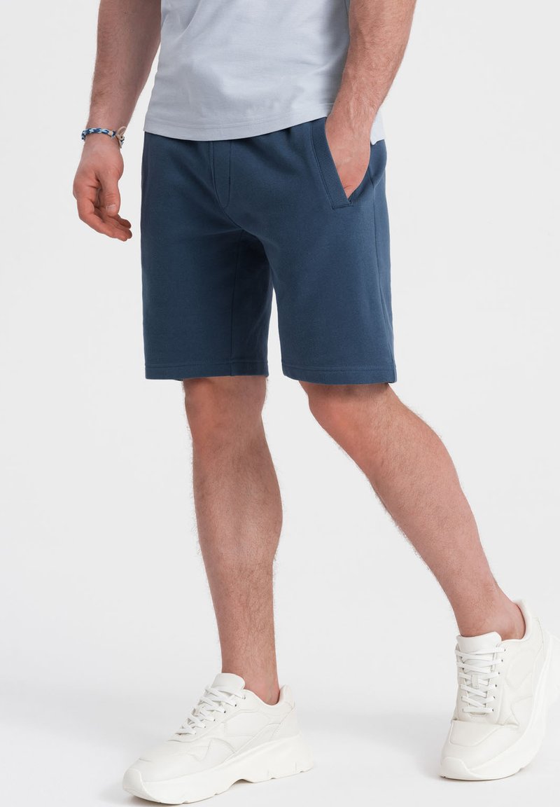 Pantaloni corti casual blu navy realizzati in tessuto morbido, dotati di tasche laterali e cintura elastica. Abbinati a sneakers bianche.