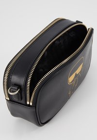 Borsa in pelle nera con zipper oro e design cartoon. Interno con rivestimento nero texturizzato. Forma compatta e rettangolare.