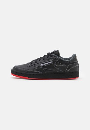 Sort Reebok lavtop-sneaker med hvide stikninger, sorte snørebånd og rød såldetalje, vist fra siden på en hvid baggrund.