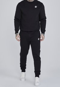 Zwarte katoenen sweatshirt en joggingbroek set. Het sweatshirt heeft een ronde hals en een klein wit logo. De joggingbroek heeft elastische boorden en een elastische tailleband.