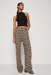 Crop top noir à rayures avec ourlet festonné associé à un pantalon large à taille haute en imprimé léopard. Tissu lisse et coupe décontractée.