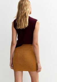 Top sin mangas color burdeos combinado con una falda corta acanalada color mostaza, que presenta un diseño ajustado y una textura suave.