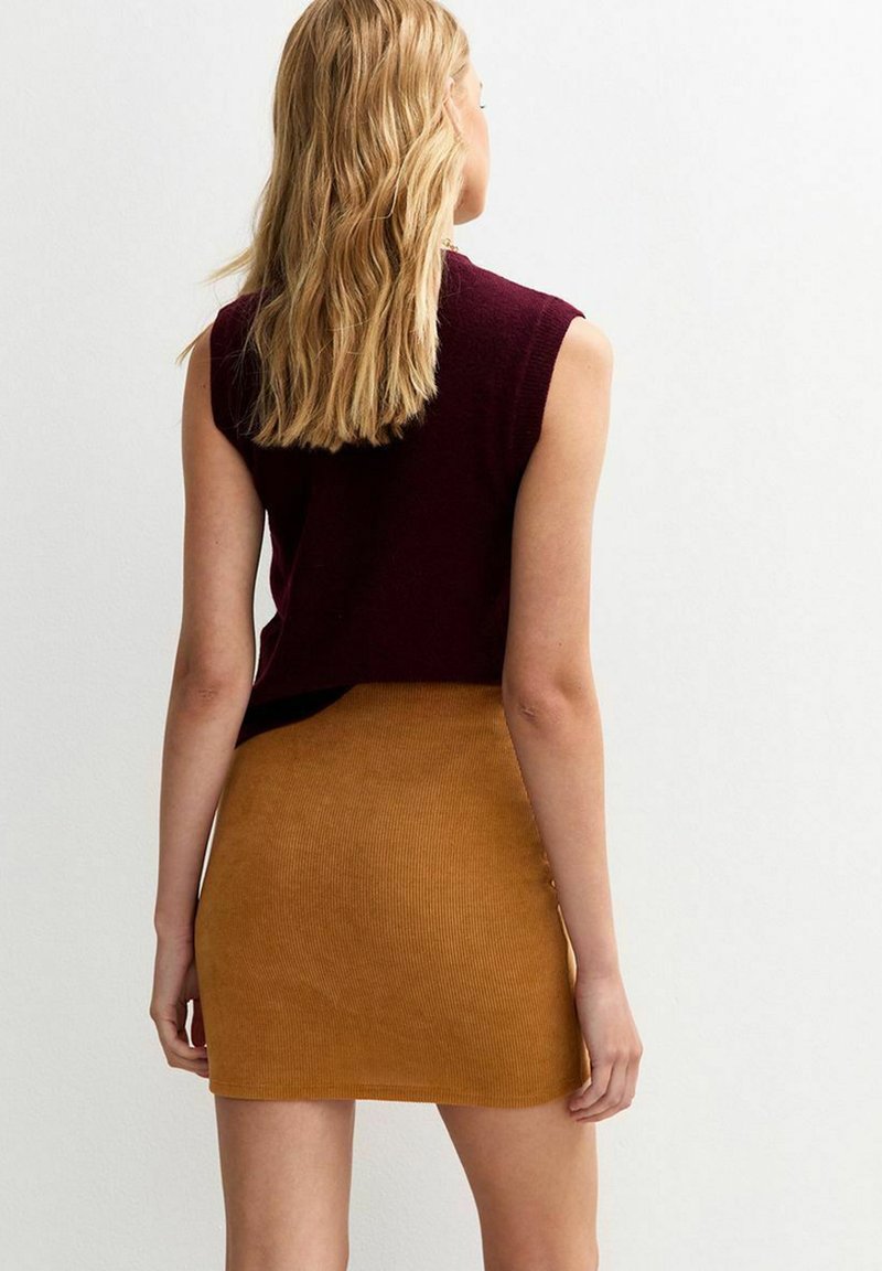 Top sin mangas color burdeos combinado con una falda corta acanalada color mostaza, que presenta un diseño ajustado y una textura suave.