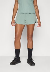 Green athletic shorts with side slits, paired with black socks and black sneakers. The shirt is a light green, ribbed material.