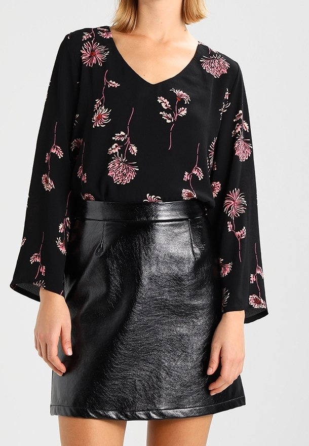 Blouse noire à motifs floraux avec de longues manches évasées, ornée de motifs floraux roses. Associée à une mini-jupe noire brillante en simili cuir.