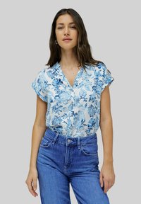 Blusa a manica corta in tessuto azzurro con motivo floreale. Design a scollo a V con bottoni, abbinata a jeans blu a vita alta.
