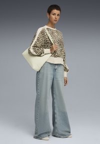 Pull en imprimé léopard avec manches longues, accents crème, associé à un jean large bleu clair et un tote bag vert pâle.