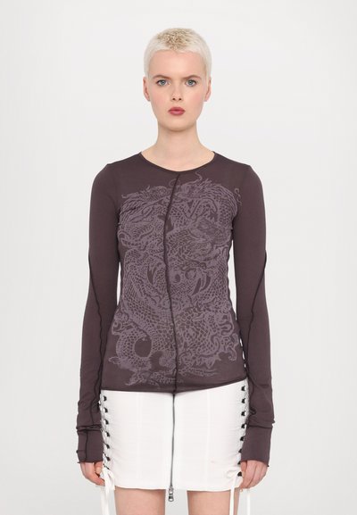 Long-sleeve, dark purple top with a dragon graphic print, featuring a front zip closure and fitted style, paired with a white zip skirt.