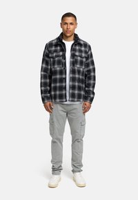 Sort og hvid ternet jakke med to brystlommer, over en hvid T-shirt. Grå cargo bukser og hvide sneakers fuldender outfittet.