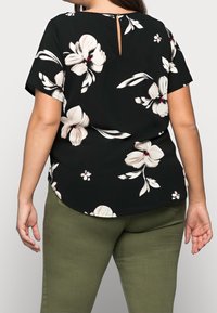 Svart blommig blus med korta ärmar, prydd med stora krämfärgade och rosa blommor, med en nyckelhålsdetalj bak, i kombination med olivgröna byxor.