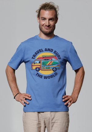 Blauwe katoenen t-shirt met een kleurrafische afbeelding van een camper met surfplanken. Tekst luidt "REIS EN SURF DE WERELD" in vette letters.