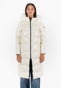 Giacca bianca lunga e gonfiosa realizzata in materiale lucido, con cappuccio rifinito in pelliccia sintetica, chiusura frontale a zip e tasche laterali.