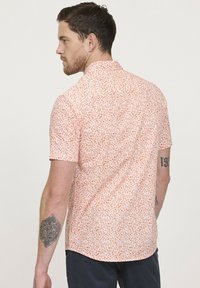 Korte mouwen shirt in lichtroze met een verspreid bloemmotief in oranje. Beschikt over een button-down kraag en een gebogen zoom.