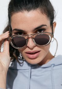 Selged tumedate läätsedega ja selge, nurgelise plastraamiga, hoitakse käes. Taust on hele ja neutraalne.