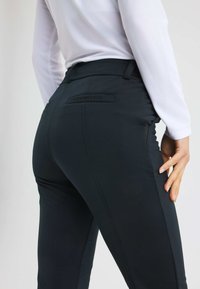 Zwarte, getailleerde broek met een gladde textuur, voorzien van een gestikt ontwerp en een zichtbaar logo op de achterste tailleband.