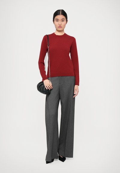 Red fitted long-sleeve sweater paired with high-waisted grey wide-leg trousers, featuring a small black handbag with a chain strap.