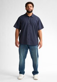 Kortärmad marinblå skjorta med knappar i bomullsblandning, kombinerad med ljusblå denimjeans och vita sneakers. Avslappnad passform, minimalistisk design.
