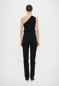 Zwarte gebreide top met één schouder, gecombineerd met tailored zwarte broeken. Gladde textuur met een aansluitend ontwerp en een slanke silhouet. Hakken vergroten de lengte.