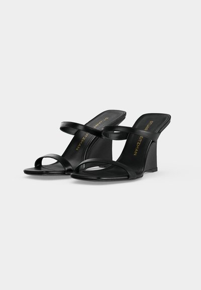 Sandales à talons noires avec deux fines brides sur le pied et orteils ouverts, avec un talon bloc incurvé et un logo doré Stuart Weitzman à l'intérieur.