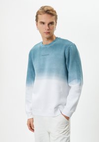 Felpa con gradiente blu chiaro a bianco, con scollatura rotonda e maniche lunghe. Presenta la scritta "POSITIVE VIBES" sul davanti. Tessuto morbido.