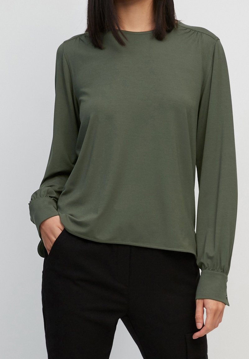 Top a maniche lunghe verde oliva in tessuto morbido con vestibilità rilassata, caratterizzato da dettagli arricciati sulle spalle e polsini con bottoni.