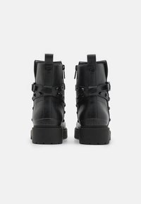 Botas de tobillo de imitación de cuero negro con tachuelas, cierre con cremallera trasera y correas ajustables; con un acabado texturizado y una suela de goma gruesa.