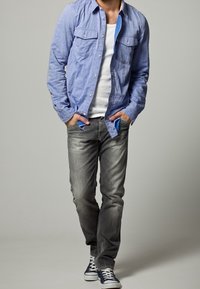 Ljusblå skjorta med knapp-up över en vit T-shirt, kombinerad med urtvättade grå jeans och marinblå sneakers. Skjortan har två bröstfickor och en avslappnad passform.