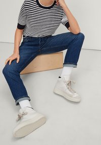 Zapatillas altas blancas con acentos en beige, llevadas con unos vaqueros de mezclilla azul y un suéter de punto a rayas en blanco y negro. Los vaqueros están remangados en los puños.