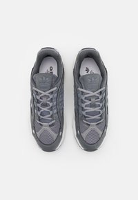 Grå träningsskor med övre del i mesh och syntetmaterial, som har tre tonalt matchande ränder, runt snörning och en vadderad krage för komfort.