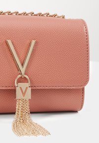 Rosa texturerad läderhandväska med en framträdande guldfärgad "V"-emblem och kedja med tofsdetalj, prydd med guldhardware-accenter.