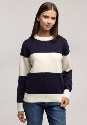 Sweter w poziome paski w kolorze granatowym i kremowym, okrągły dekolt, ściągacze na rękawach. Noszony z niebieskimi dżinsami o luźnym kroju.