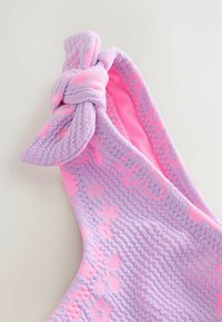 Bandeau en tricot de couleur violet clair avec des accents roses. Il présente un détail en nœud en haut et un tissu texturé avec un motif.