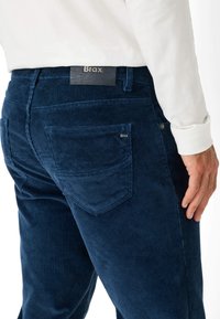 Marineblauwe corduroybroek met ribbelstructuur, vijf-pocket ontwerp en een leren label met het "Brax" logo op de tailleband.