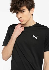 Sort T-shirt lavet af glat stof med et hvidt Puma-logo på venstre bryst. Korte ærmer og rund halsudskæring.