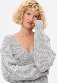 Jasnoszary sweter dziergany z głębokim dekoltem w kształcie litery V i oversize'owymi rękawami. Miękka tekstura, z luźnym krojem i ściągaczami przy mankietach.