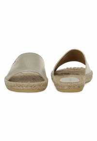 Et par guld slip-on sandaler med vævet jutesåler og brede frontstropper, vist fra fronten på hvid baggrund.