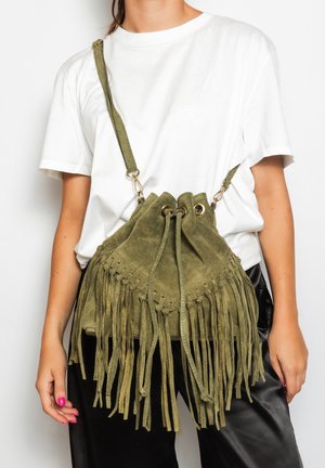 Borsa a secchiello in camoscio verde oliva con frange, chiusura con coulisse e dettagli metallici; indossata a tracolla con spallaccio regolabile.