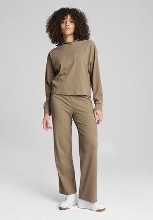 Sudadera marrón con canalé, capucha y pantalones a juego, ambos con un ajuste relajado. Zapatillas blancas con suelas texturizadas completan el conjunto.