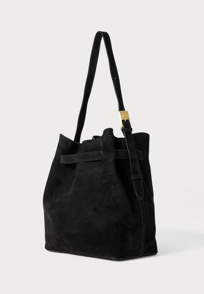Black suede bucket bag with a single long strap, adjustable buckle, and soft texture; features a slouchy silhouette and minimal design.