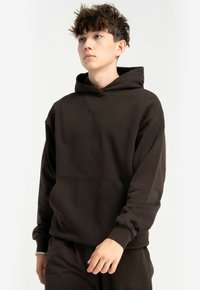 Brązowy hoodie wykonany z bawełny, z przednią kieszenią, długimi rękawami i kapturem ze sznurkiem. Gładka tekstura i luźny krój.
