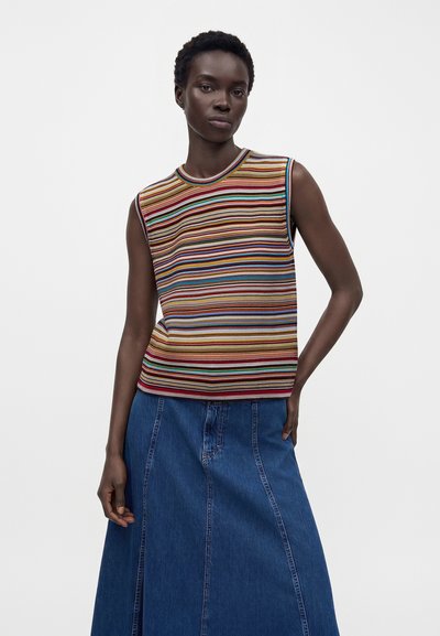 Femme portant un haut sans manches rayé multicolore et une jupe en jean bleu taille haute, debout avec une main dans la poche.