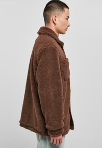 Brun fleecejakke med krave, sidelomme og tekstureret, fluffy stof. L�øs pasform med let faldende skuldre og lige kant.