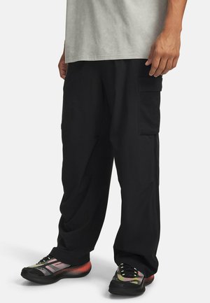 Zwarte cargobroek met losse pasvorm, voorzien van zijzakken en een gladde textuur, gecombineerd met meerkleurige sportschoenen.