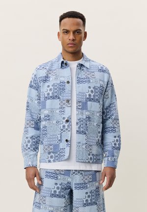 Man wearing matching light blue patterned jacket and shorts over a white T-shirt, standing against plain background.