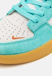 Turkos sneaker med en ovandel i mocka och perforerade detaljer, accentuerad med en orange logotyp och en strukturerad gummisula.