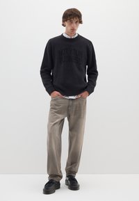 Schwarzer gerippter Pullover mit dem Aufdruck "NOT YOUR BUSINESS", kombiniert mit hellbraunen, lockeren Jeans und schwarzen Plattformschuhen.