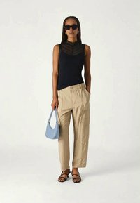 Black sleeveless top with lace detail, beige cargo pants, black sandals, and a small blue handbag. Smooth textures and relaxed fit.